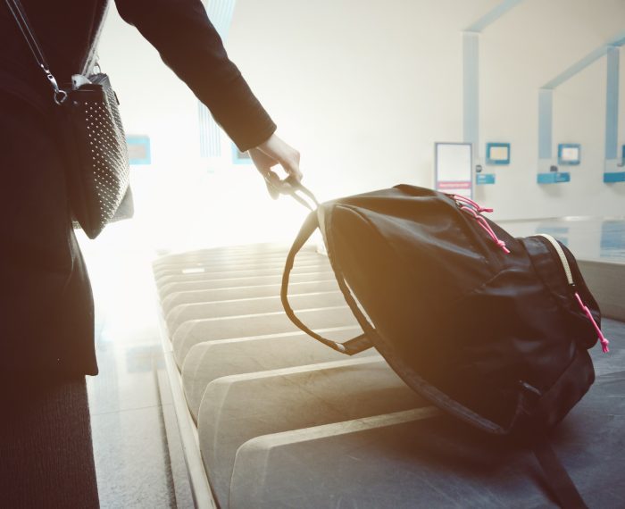 Woman taking her bag from the luggage conveyor belt in arrivals lounge of airport terminal.