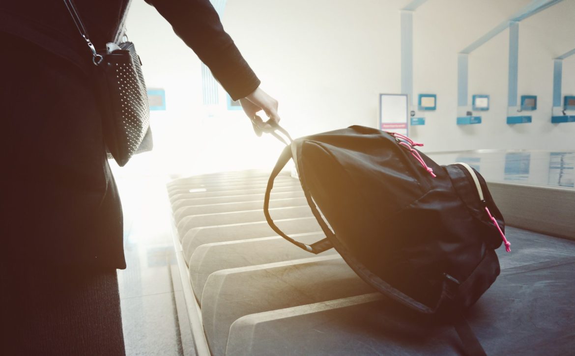 Woman taking her bag from the luggage conveyor belt in arrivals lounge of airport terminal.